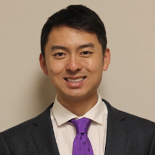 Headshot of Dr. Larry Han smiling, wearing a dark gray suit jacket, a white collared shirt, and a vibrant purple necktie
